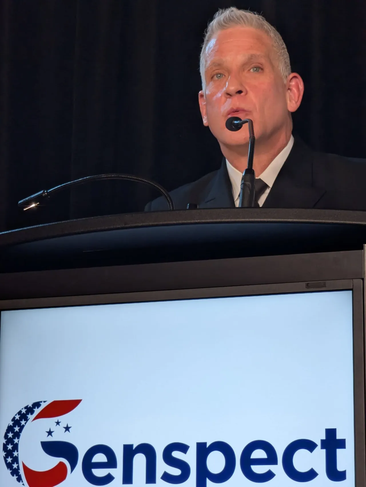 A speaker at a lectern with a Genspect screen below