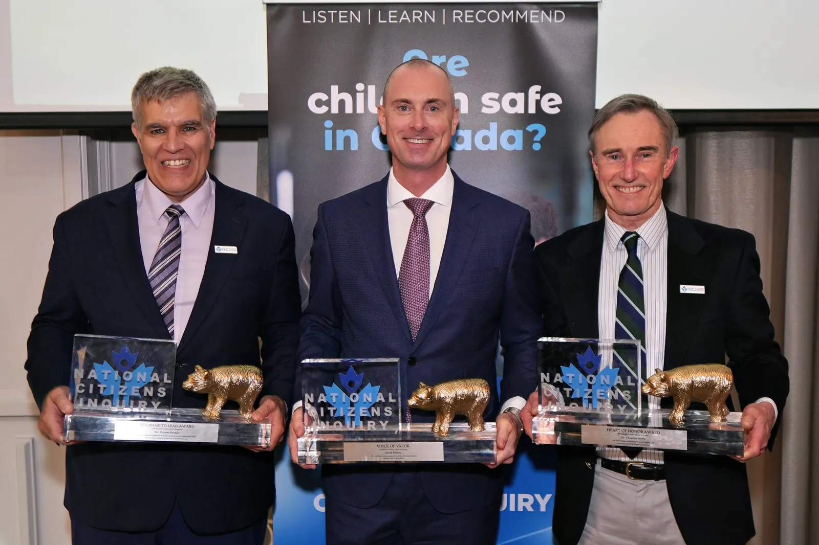 Three men in suits each holding a National Citizens Inquiry award